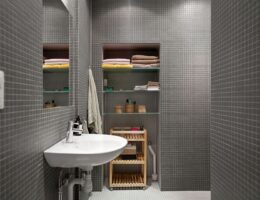 Modernt badrum med grå mosaik, handfat och en hängande handduk på väggen.
