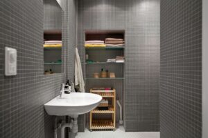 Modernt badrum med grå mosaik, handfat och en hängande handduk på väggen.