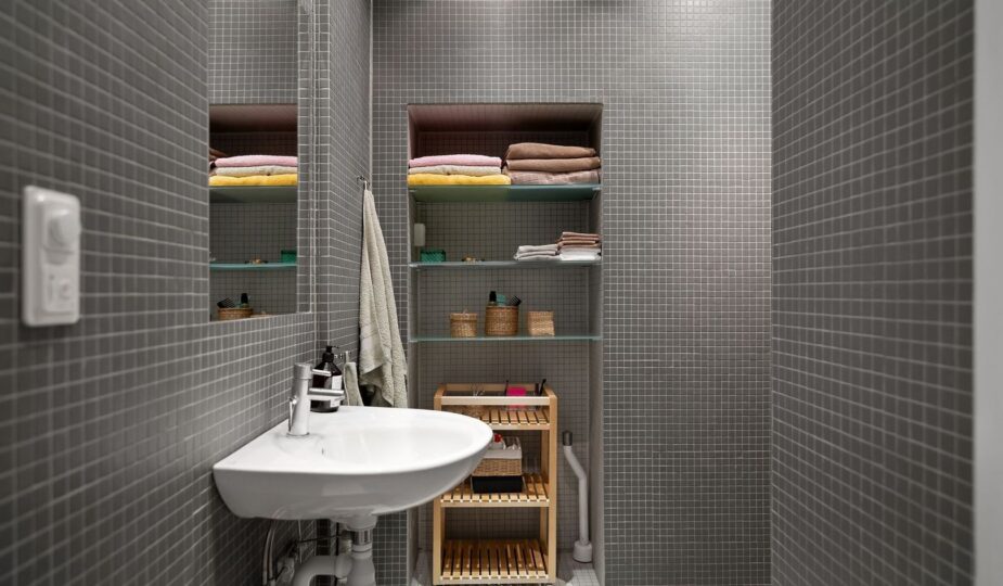 Modernt badrum med grå mosaik, handfat och en hängande handduk på väggen.