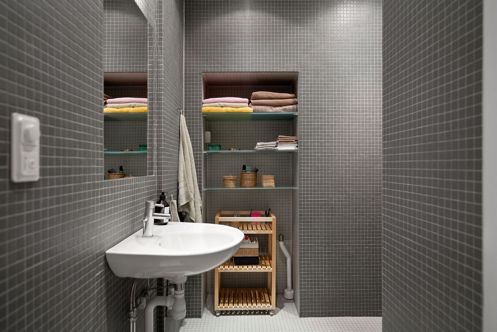 Modernt badrum med grå mosaik, handfat och en hängande handduk på väggen.
