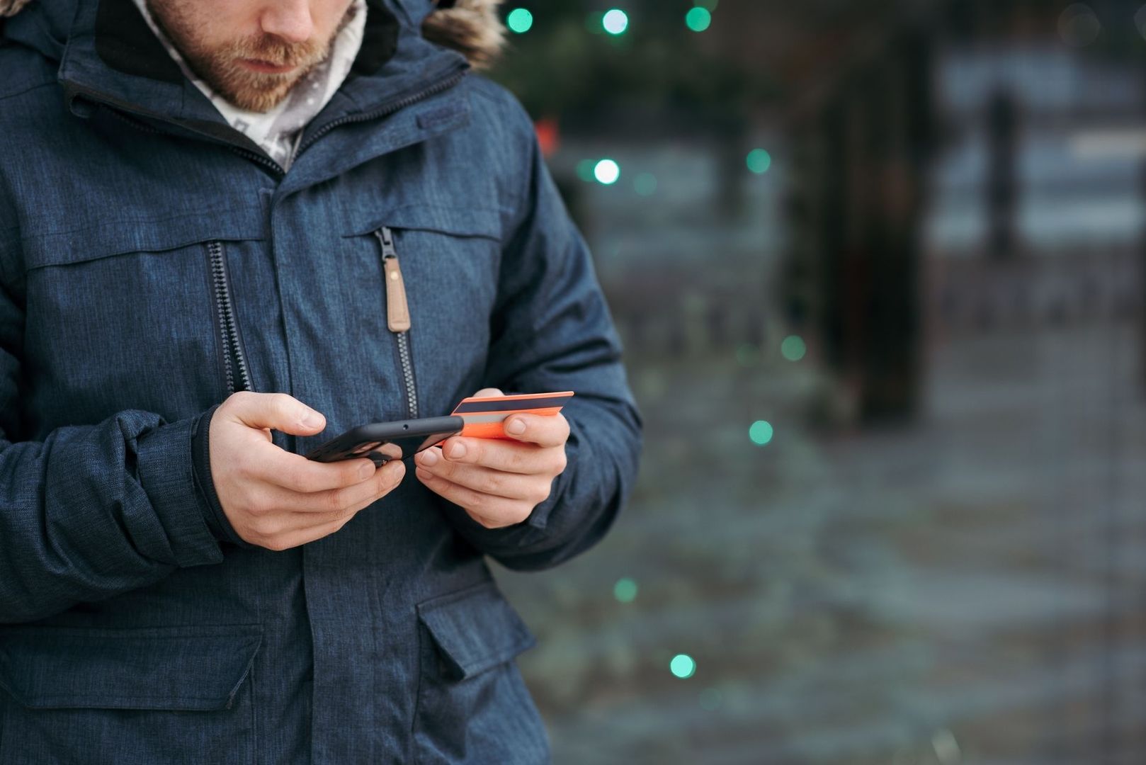 Person i vinterjacka håller en smartphone och ett orange kort