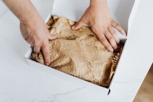 Händer packar en vara i en kartong med återvinningsbart fyllnadsmaterial